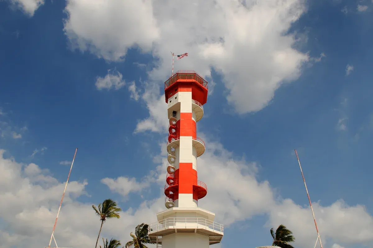 The red-and-white striped Ford Island control tower, being restored by the Pacific Aviation Museum Pearl Harbor, against a blue sky with palms, a stop on Pearl Harbor tours from Honolulu