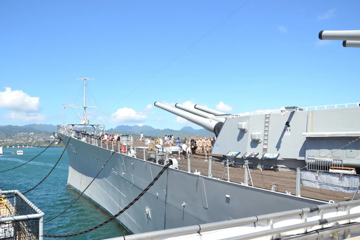 Bow and forward 16-inch turret of the battleship USS Missouri (BB-63) at Ford Island, visitors on deck, harbor and Koolau hills behind, a stop on Pearl Harbor tours from Honolulu